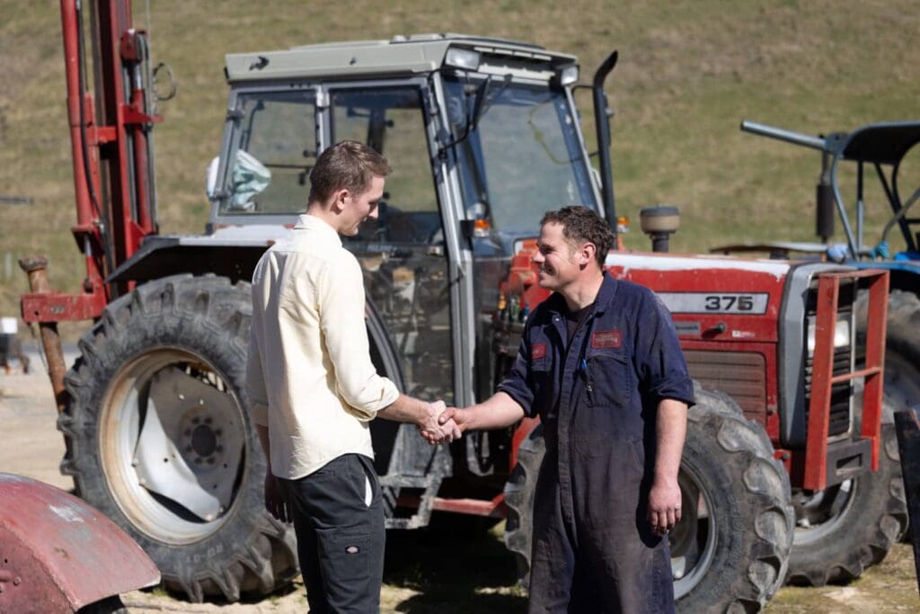Casey from ProPart handshaking with a customer standing in front of a red tractor