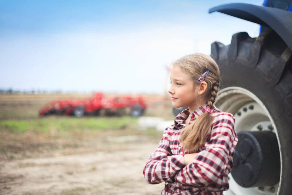 Young girl standing by tractor wheel